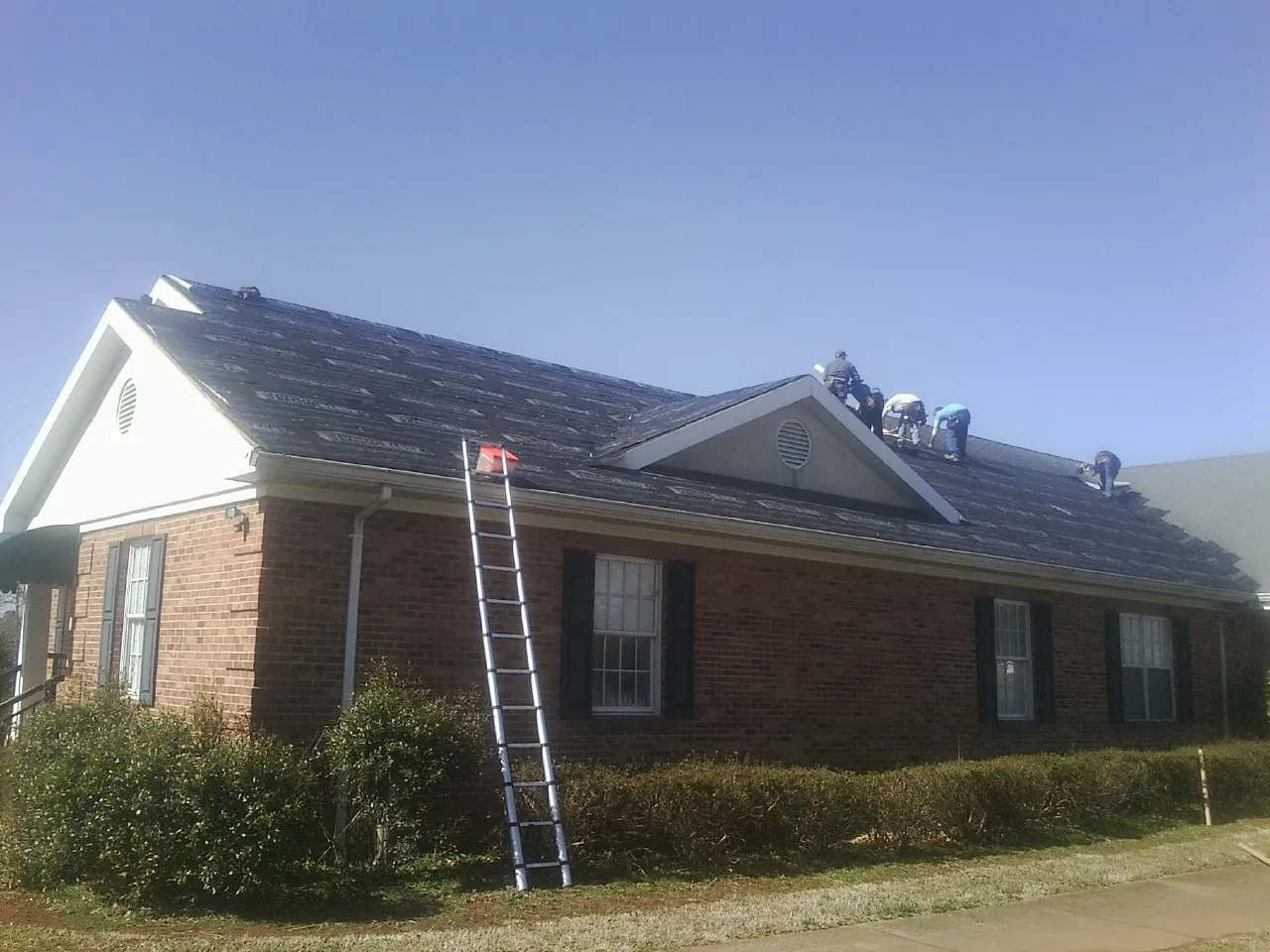 Crew tearing shingles off a brick ranch roof with a ladder set — Emergency Roof Repair work by our crew in Slatington
