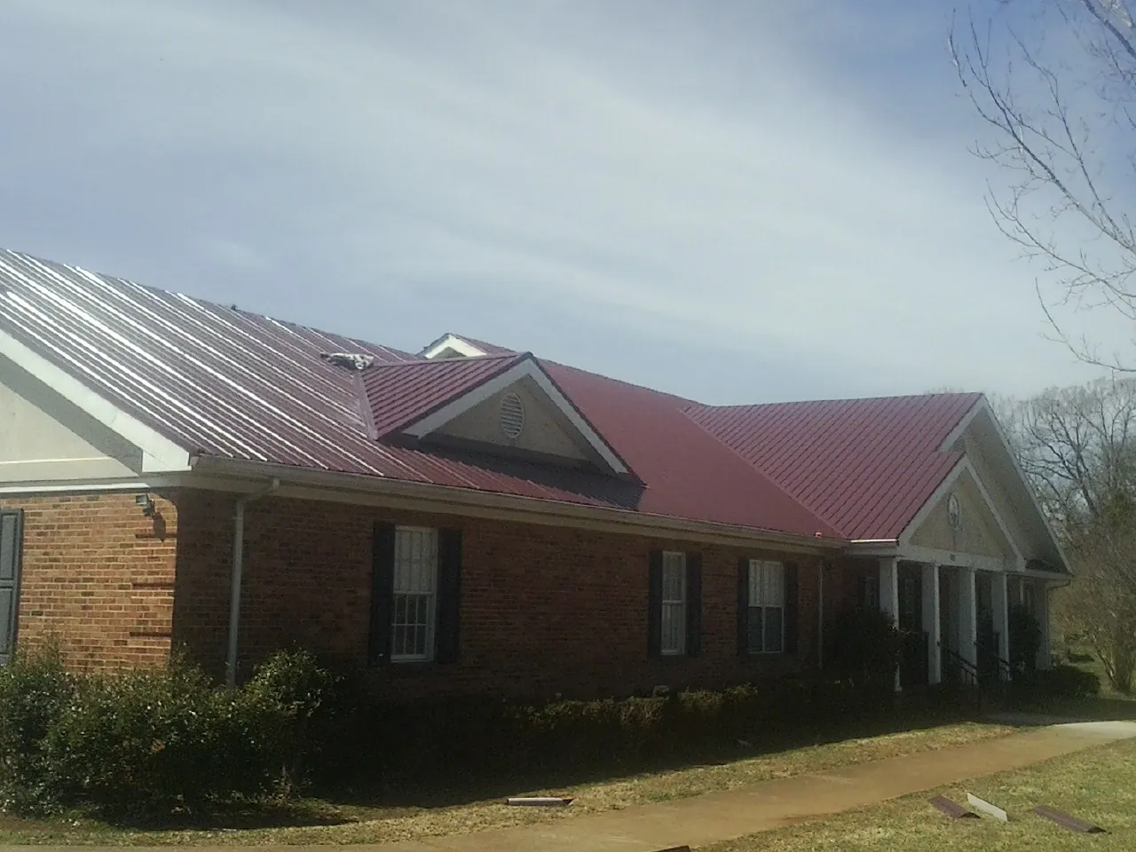 Red metal roof with gabled entries on a long brick building, from a Hail Damage Roof Repair job in Slatington