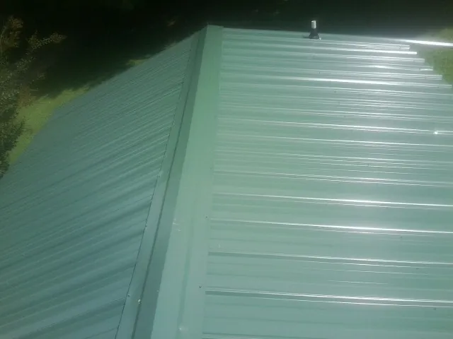 New green metal panels meeting at the ridge of a roof — Flat Roof Repair work by our crew in Slatington