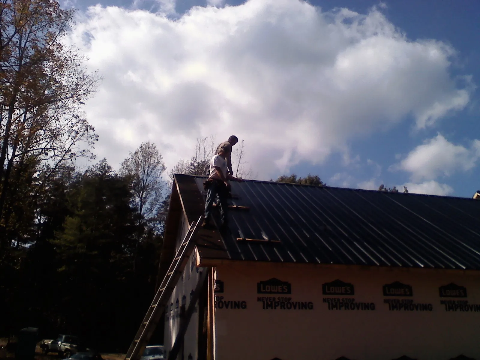 Roofer fastening dark metal panels high against a cloudy sky, from a Roof Inspection job in Slatington