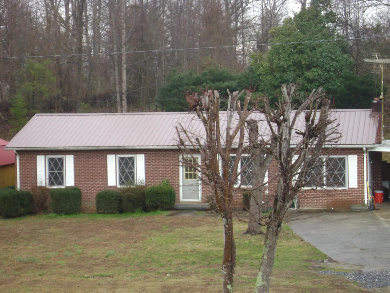Mauve metal roof on a brick ranch home behind bare trees in Slatington