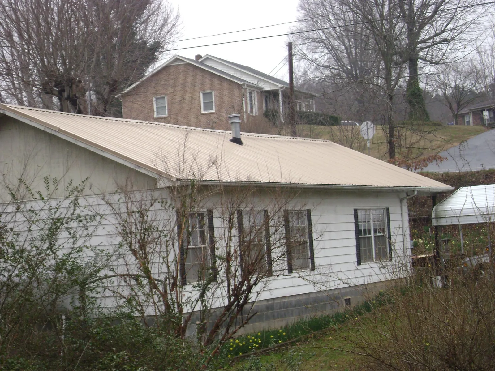 Tan metal roof on a white sided house set into a hillside — Commercial Roofing by Roofing Brothers in Slatington